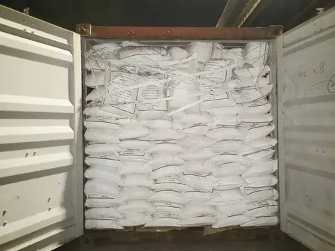 Open shipping container stacked to the roof with white 30 kg bags held in place by lashing straps